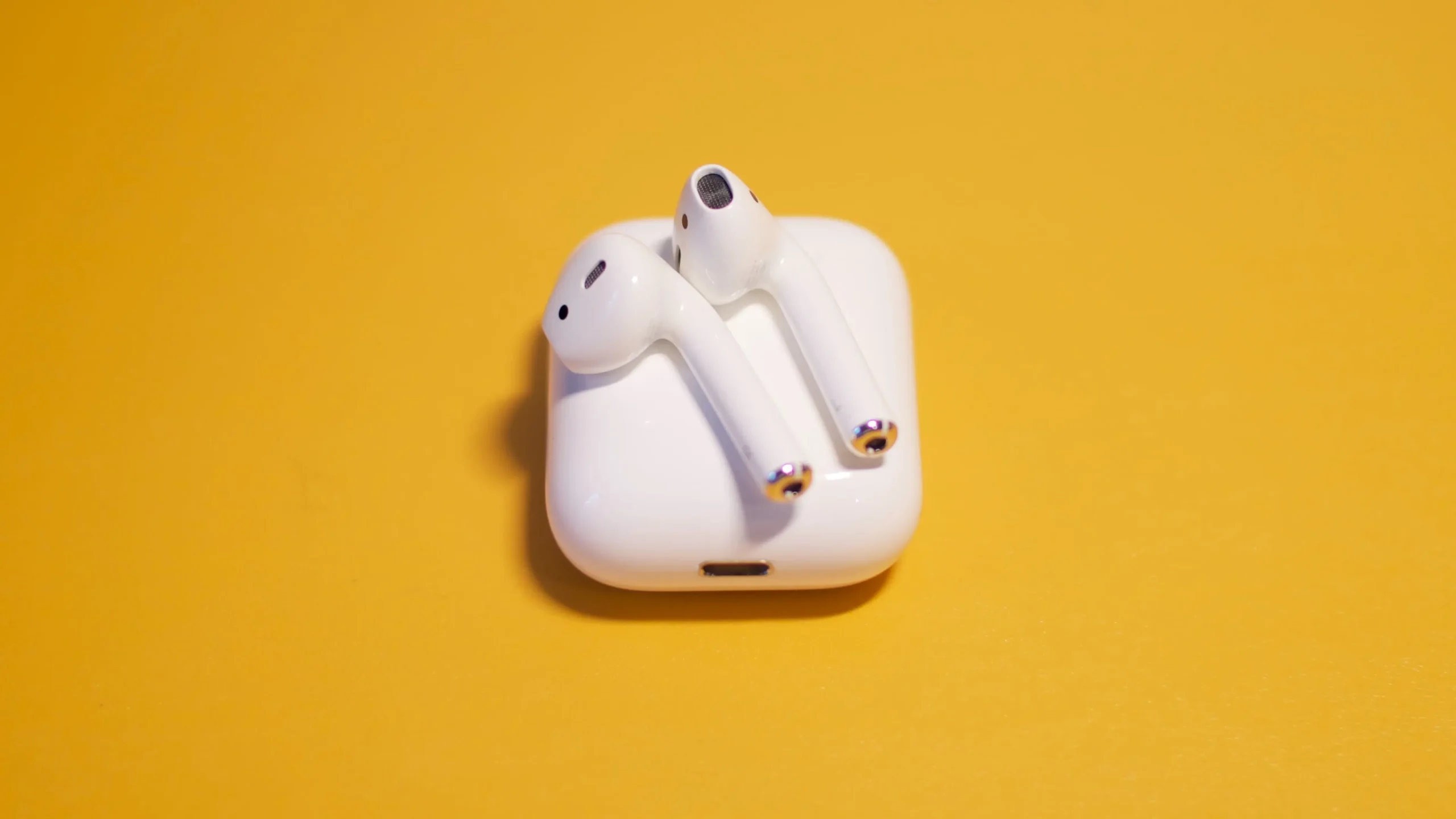 Apple AirPods resting on their charging case, set against a yellow solid background