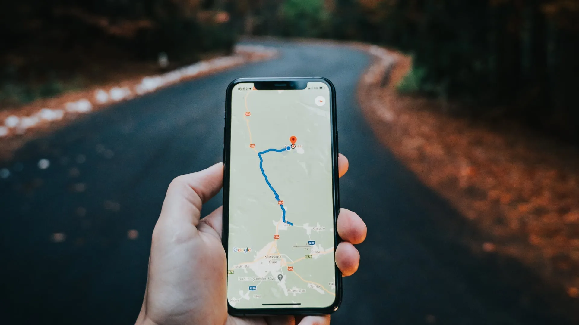 iPhone в руке мужчины в лесу, отображает навигационные указания на Картах Google