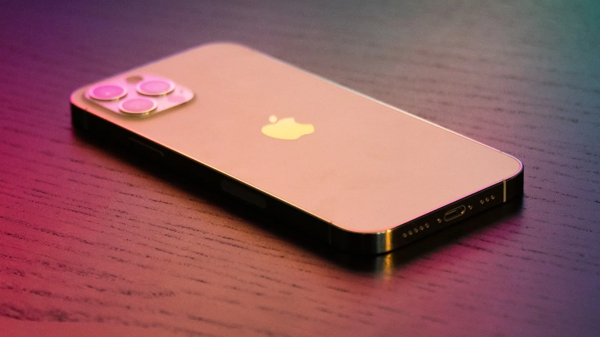 iPhone 12 Pro color oro sotto un'illuminazione colorata, appoggiato a faccia in giù su un tavolo di legno