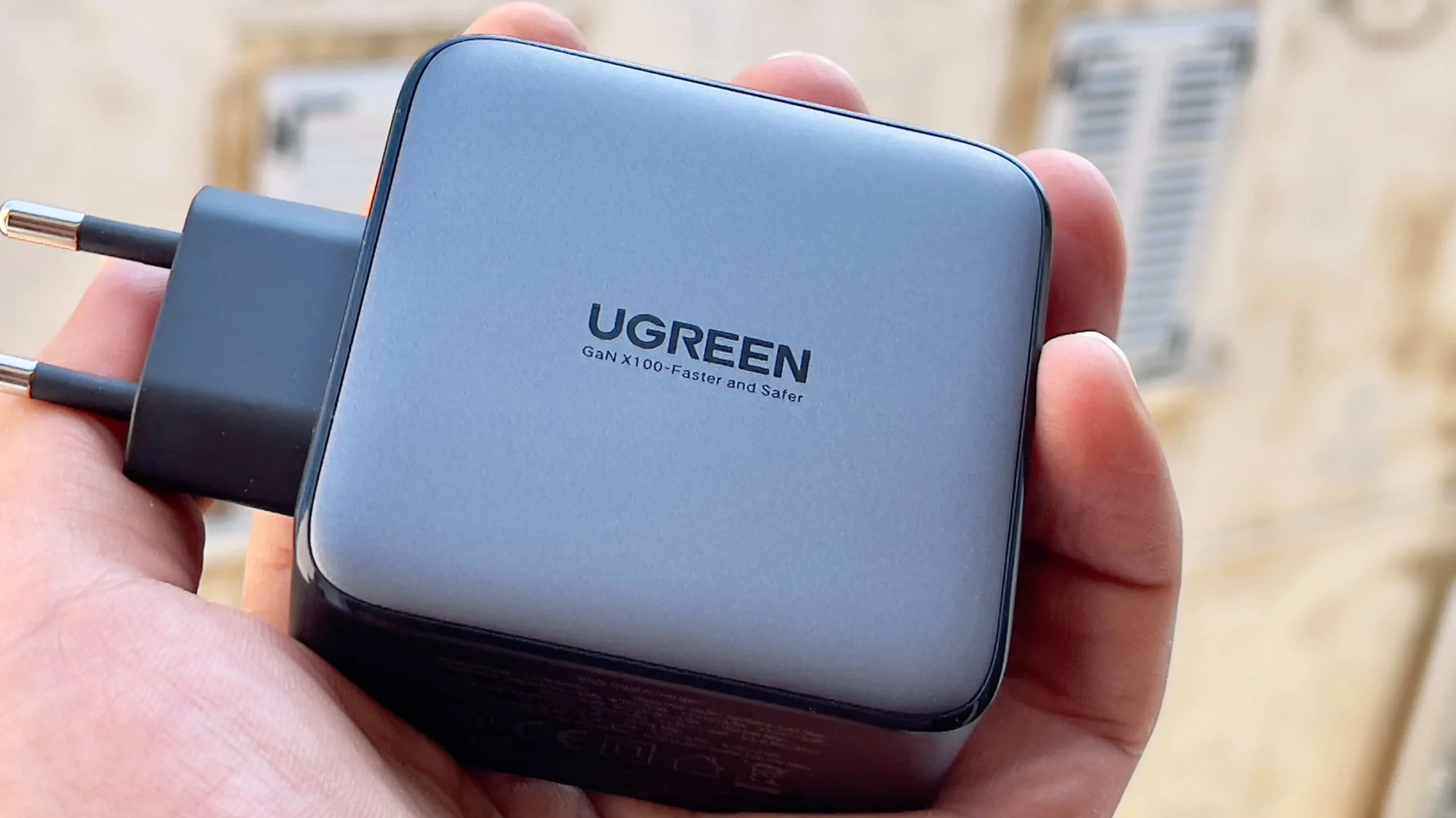 Мужчина держит в руке 100-ваттный адаптер питания Nexus от Ugreen и демонстрирует логотип Ugreen со слоганом.
