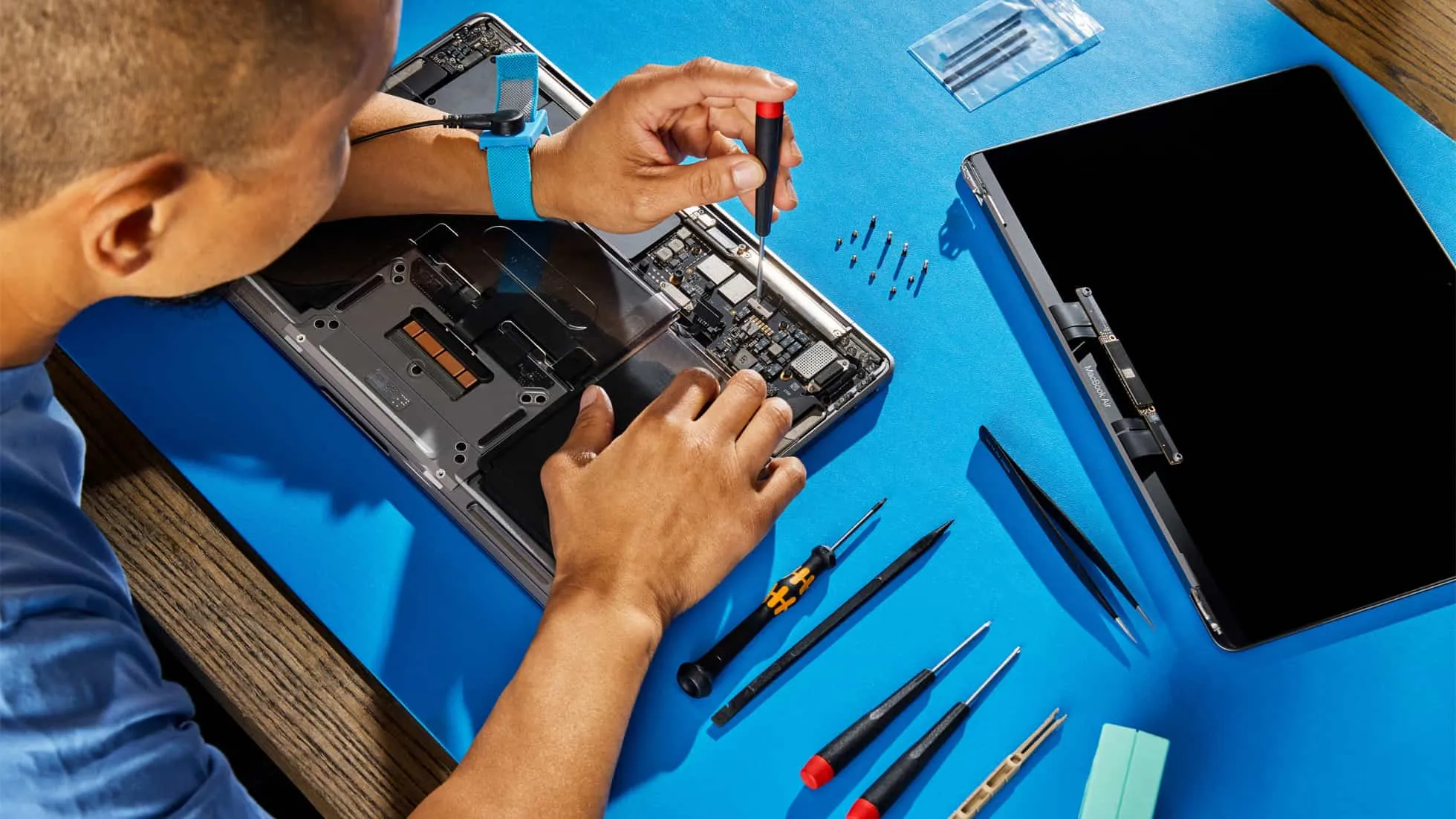 A customer hunched over their table, using genuine Apple parts, tools and manuals to repair a broken MacBook Pro A customer hunched over their table, using genuine Apple parts, tools and manuals to repair a broken MacBook Pro