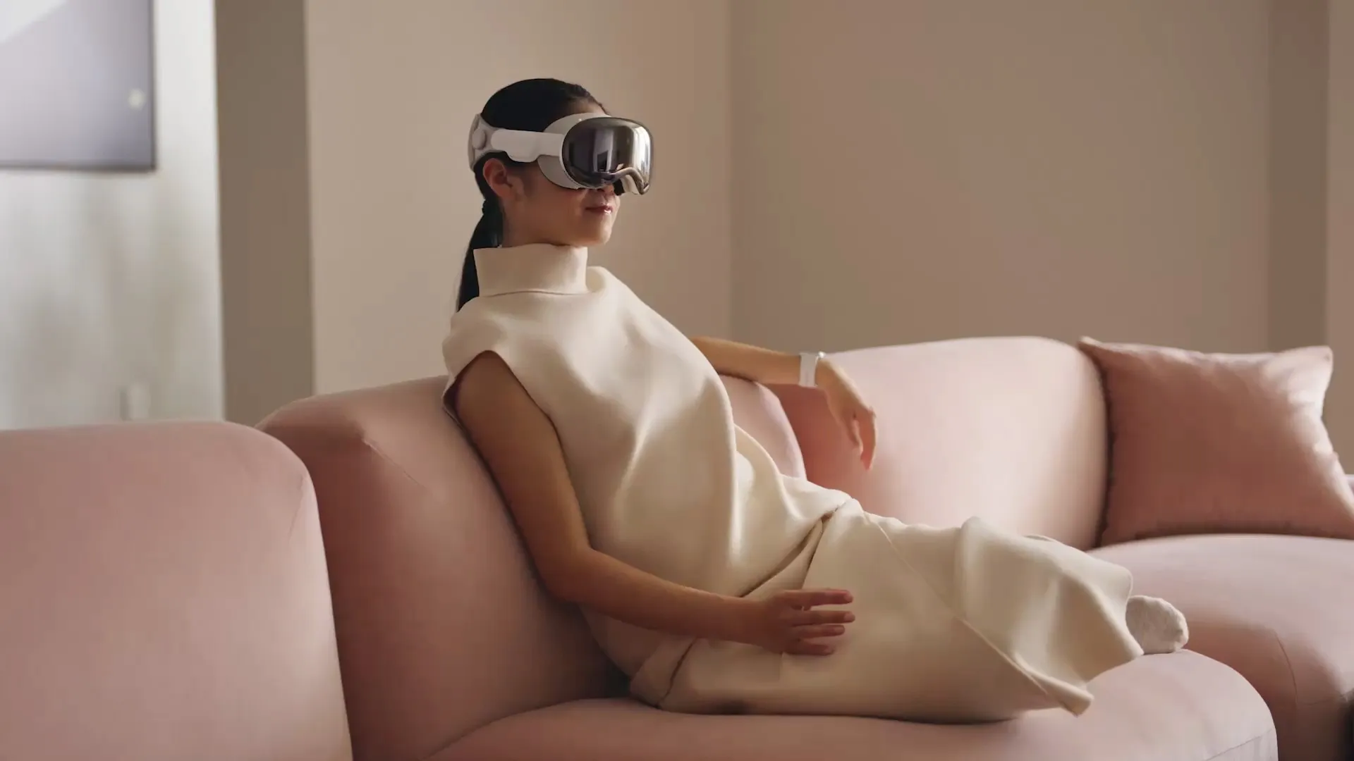 Frau sitzt auf einer Couch, trägt das Vision Pro-Headset von Apple und macht Handgesten