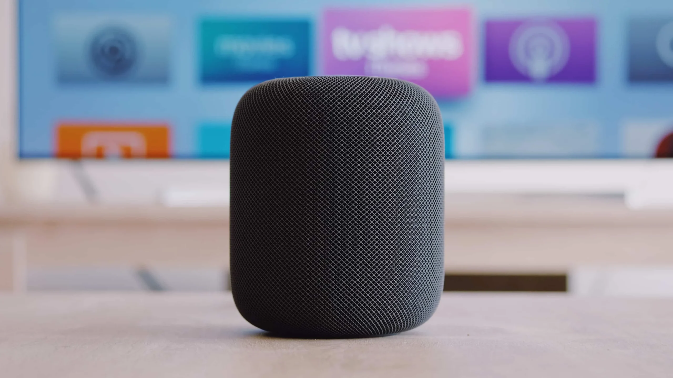 Apple TV 홈 화면을 표시하는 TV 세트 앞 테이블 위에 놓여 있는 검은색 Apple HomePod 무선 스피커