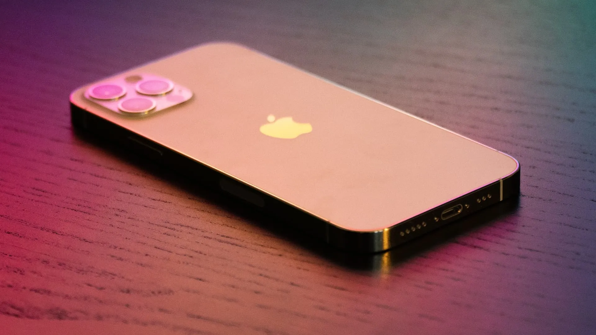 Goldenes iPhone 12 Pro unter bunter Beleuchtung, verdeckt auf einem Holztisch