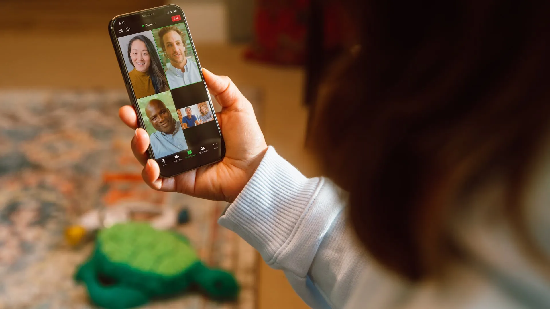 Una donna in salotto partecipa a una videochiamata Zoom sul suo telefono con altre quattro persone
