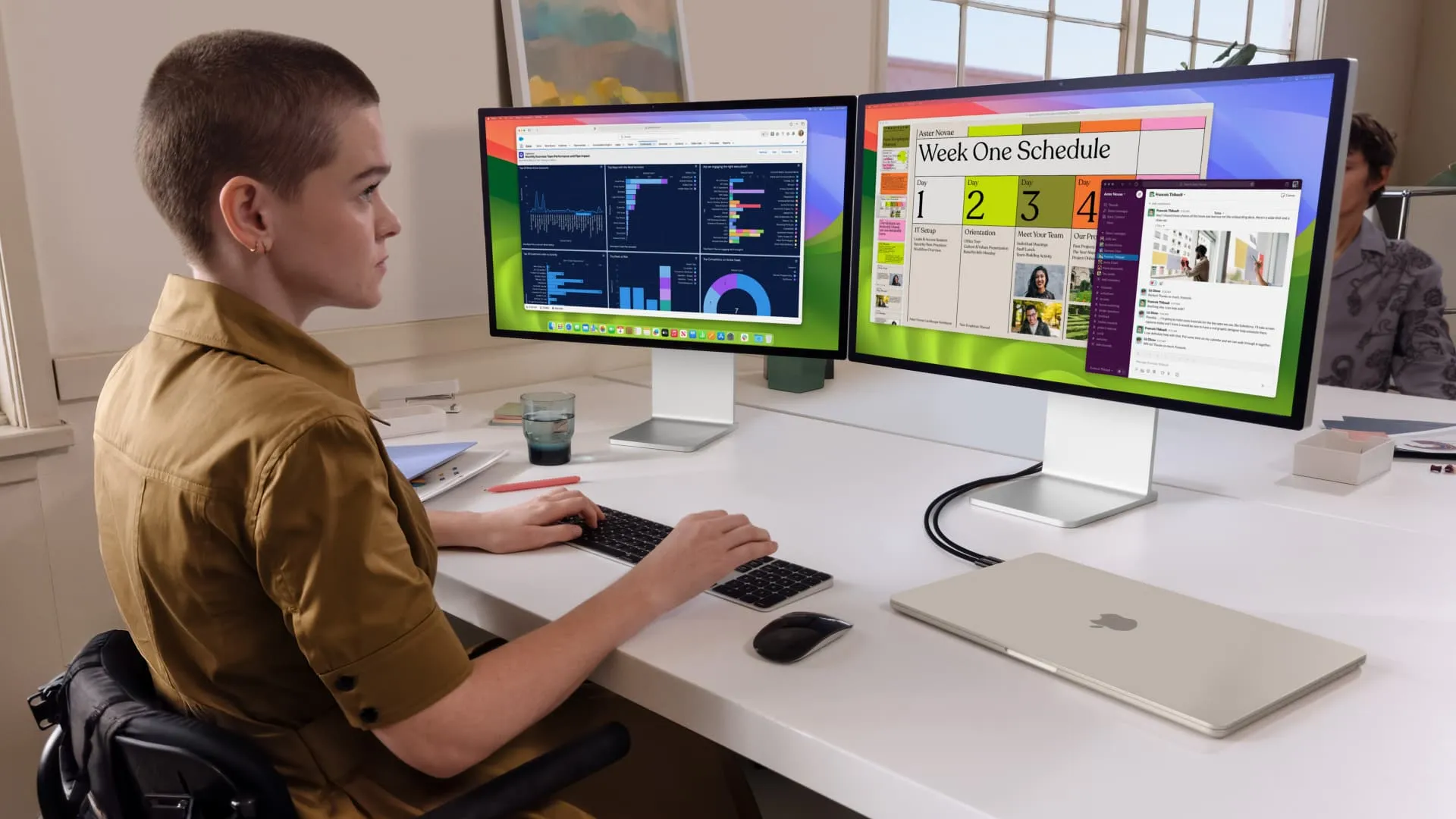 Молода людина сидить за столом і працює на M3 MacBook Air, підключеному до двох зовнішніх дисплеїв у режимі розкладачки