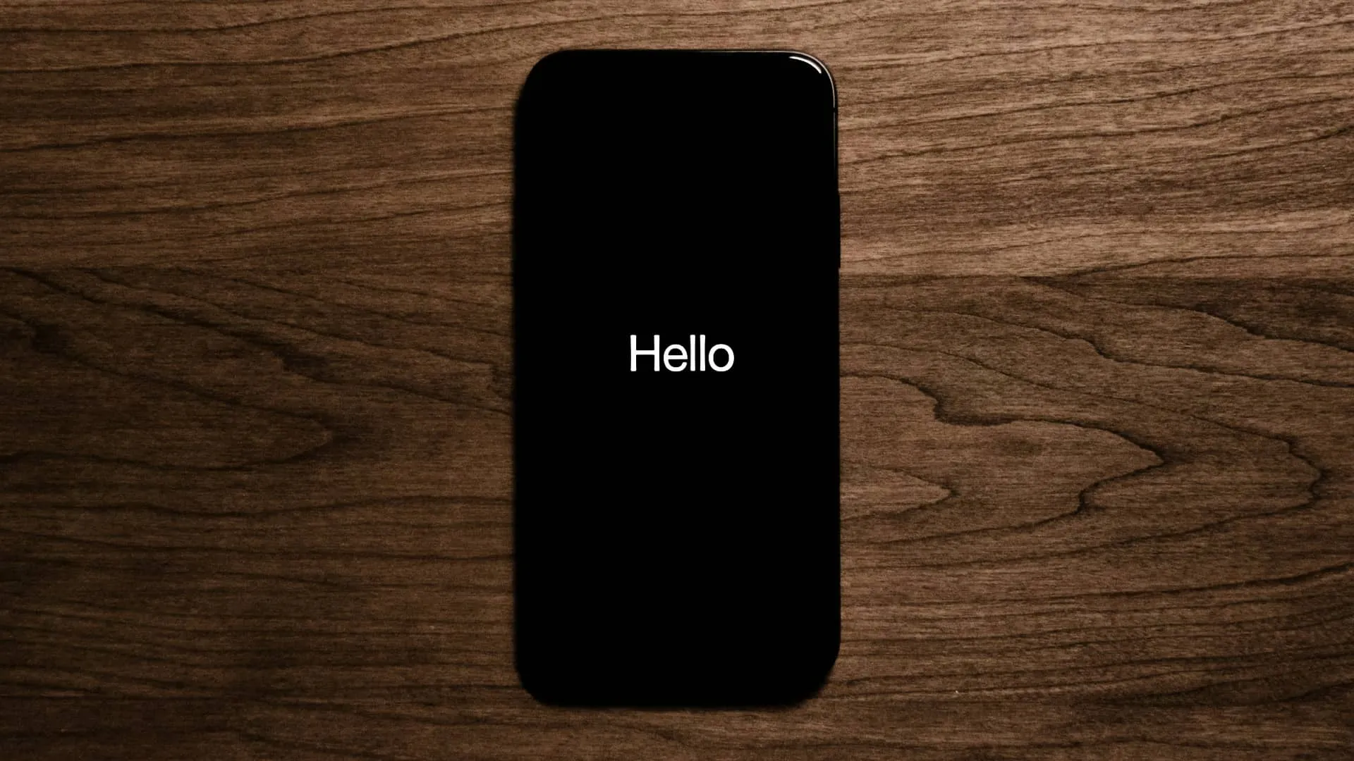 iPhone на дерев’яній поверхні, на екрані відображається повідомлення «Привіт».