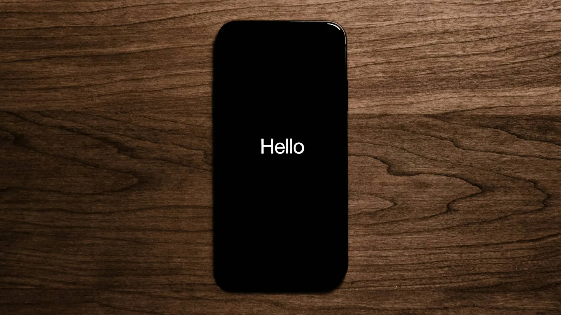 iPhone na dřevěném povrchu, na obrazovce se zobrazuje zpráva Hello